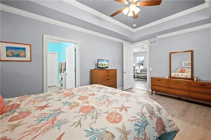 Bedroom with crown molding, light wood-style floors, a raised ceiling, and a ceiling fan