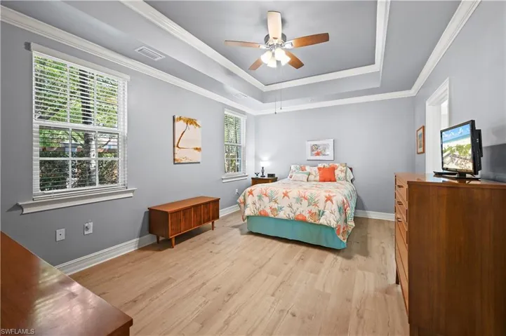 Bedroom with crown molding, light wood-style floors, and a tray ceiling