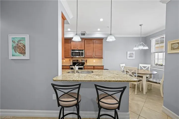 Kitchen featuring a breakfast bar area, light stone countertops, ornamental molding, appliances with stainless steel finishes, and brown cabinets