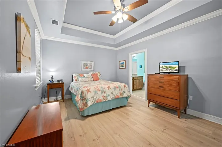 Bedroom with light wood finished floors, baseboards, a tray ceiling, and crown molding