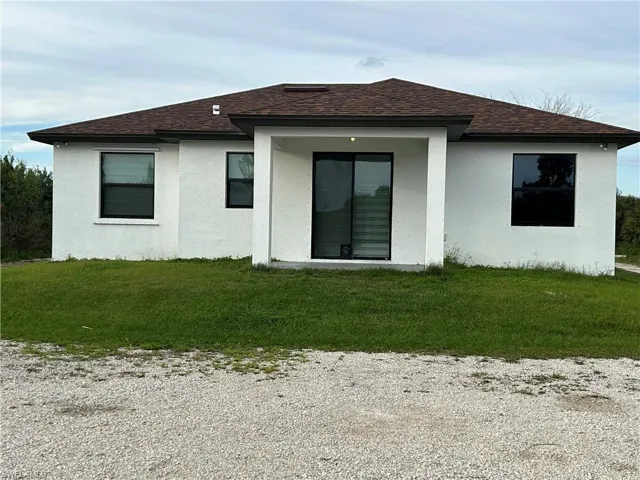 Back of property featuring a shingled roof, stucco siding, and a lawn