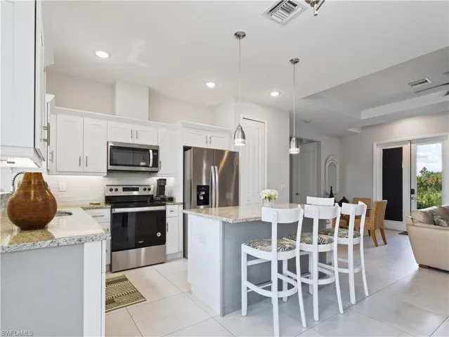 Kitchen with stainless steel appliances, light stone countertops, decorative backsplash, white cabinets, and a tray ceiling