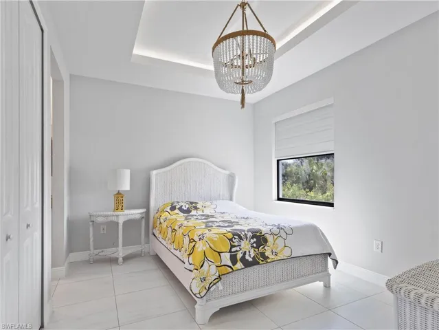 Bedroom featuring suspended lighting, a raised ceiling, a closet, and light tile patterned floors