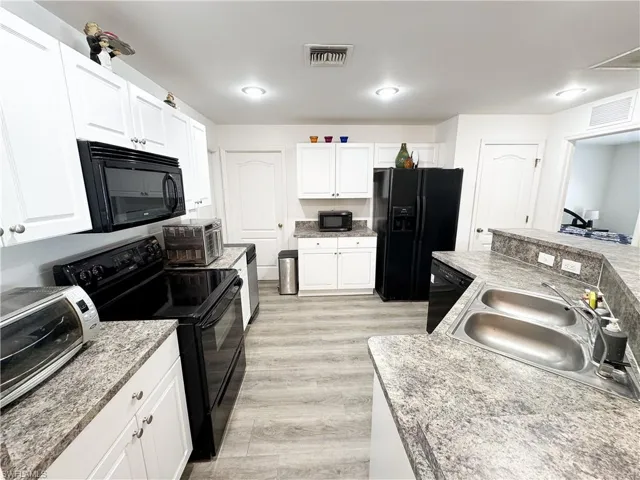 Kitchen with visible vents, light wood-style flooring, white cabinets, black appliances, and a sink