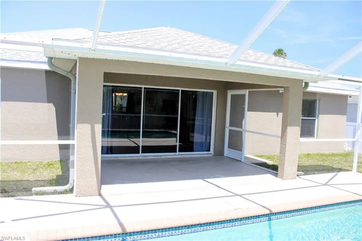 Rear view of property with roof with shingles, glass enclosure, stucco siding, a patio area, and an outdoor pool