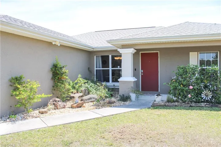 Property entrance featuring a shingled roof, a lawn, and stucco siding