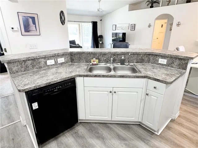 Kitchen featuring light wood finished floors, black dishwasher, white cabinetry, a ceiling fan, and a sink