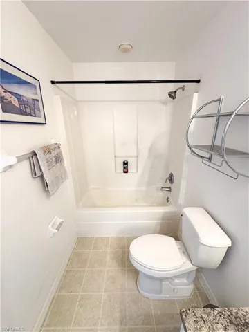 Bathroom with tile patterned flooring, toilet, bathtub / shower combination, and baseboards