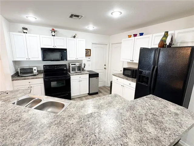 Kitchen featuring a sink, black appliances, white cabinets, and light wood-type flooring