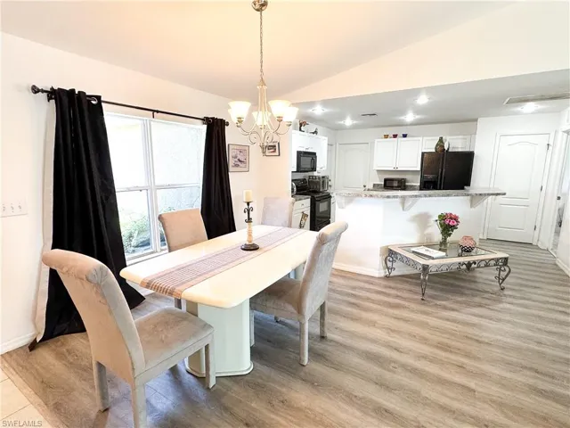 Dining space featuring baseboards, lofted ceiling, light wood-style floors, and an inviting chandelier