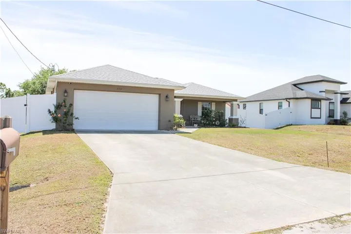 View of front facade with a front lawn, an attached garage, fence, and stucco siding