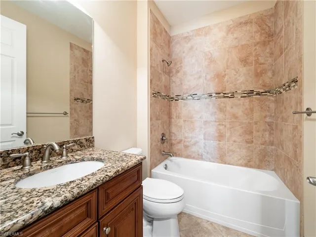 Full bathroom with tiled shower / bath combo, vanity, toilet, and tile patterned flooring