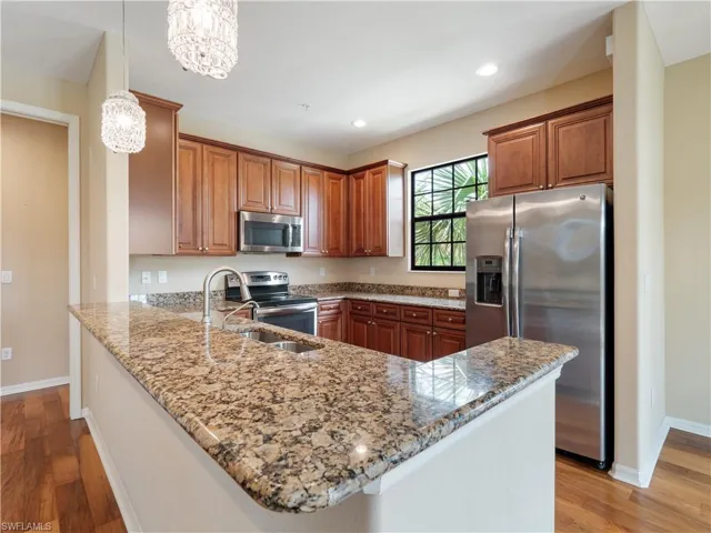 Kitchen with appliances with stainless steel finishes, light stone counters, kitchen peninsula, and decorative light fixtures