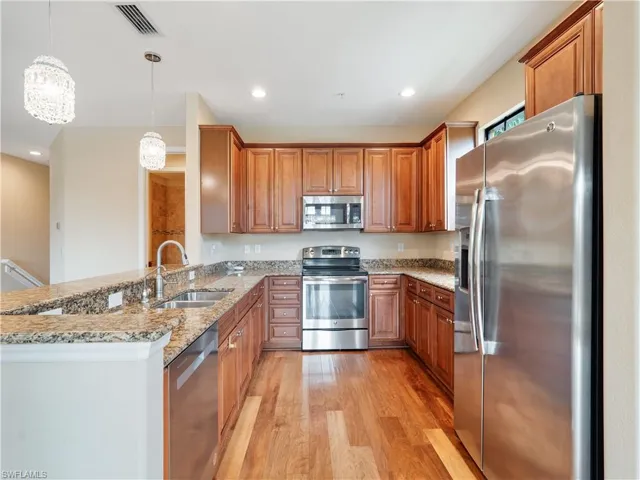 Kitchen featuring decorative light fixtures, light hardwood / wood-style floors, stainless steel appliances, sink, and kitchen peninsula