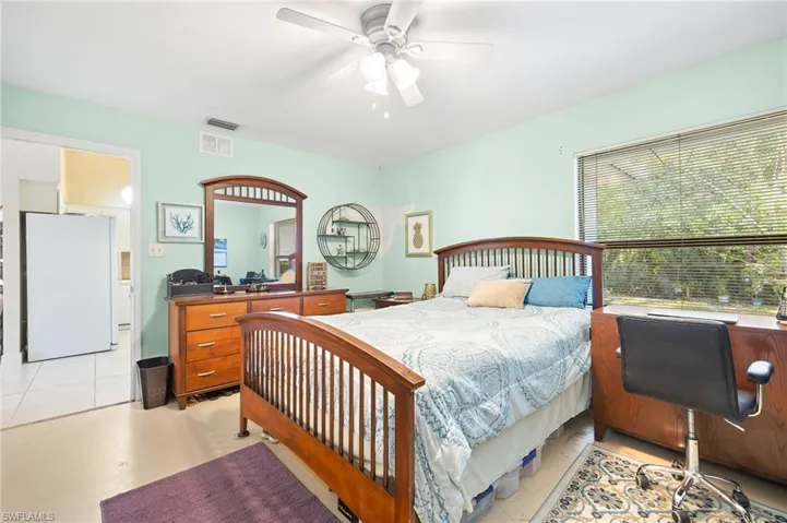 Bedroom with ceiling fan, visible vents, and freestanding refrigerator