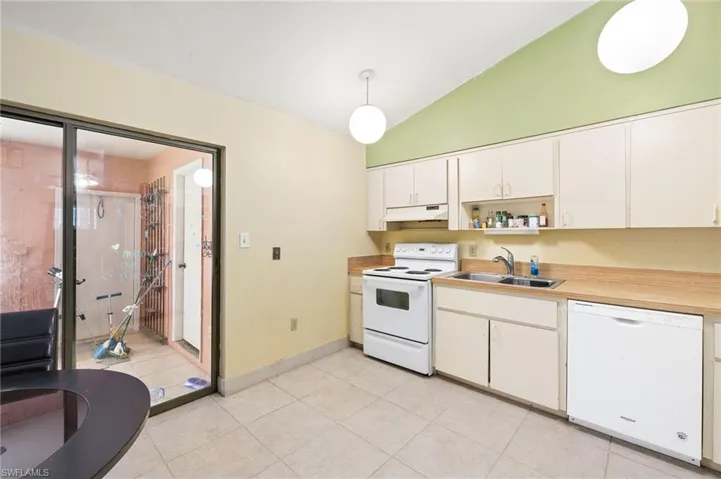 Kitchen featuring white appliances, under cabinet range hood, white cabinetry, lofted ceiling, and a sink