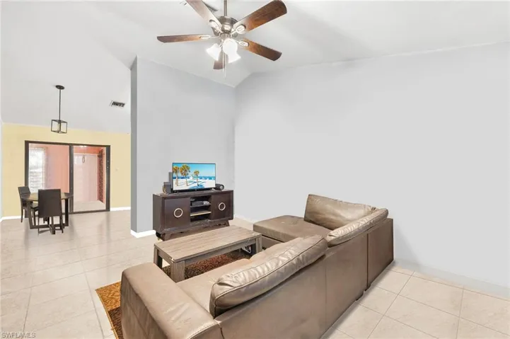 Living room featuring light tile patterned flooring, a ceiling fan, lofted ceiling, baseboards, and visible vents