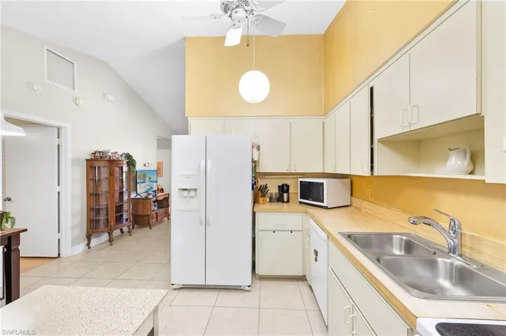 Kitchen with light countertops, a sink, light tile patterned floors, white appliances, and visible vents