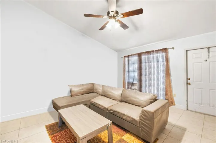 Living room featuring baseboards, vaulted ceiling, ceiling fan, and light tile patterned floors