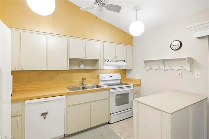 Kitchen with light countertops, white appliances, ceiling fan, under cabinet range hood, and a sink