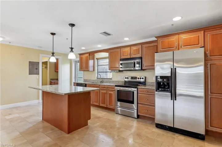 The Captiva unit kitchen featuring appliances with stainless steel finishes, light stone counters, a center island, pendant lighting, tile floors, and a sink