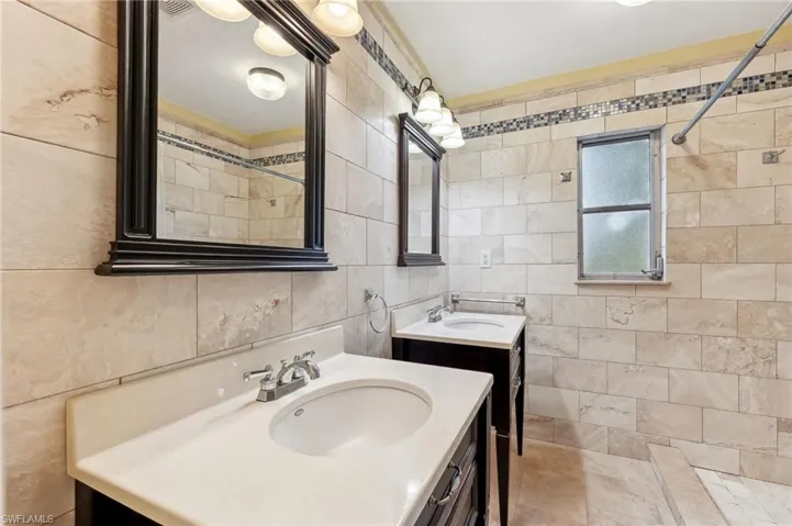 The Captiva unit guest bathroom featuring two vanities, a sink, tile walls, walk-in shower, and decorative backsplash