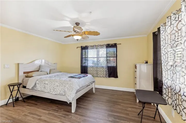 The Del Rey unit Primary Bedroom with dark wood LVT floors, crown molding, ceiling fan and baseboards