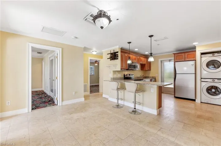 The Aruba unit kitchen featuring a breakfast bar, tile floors, appliances with stainless steel finishes, stacked washer / dryer, light stone countertops, and a peninsula