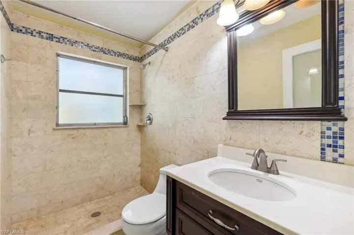 The Aruba unit full guest bathroom featuring toilet, a walk-in shower, tile walls, and vanity