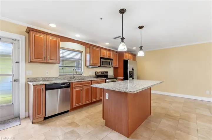 The Captiva unit kitchen featuring decorative light fixtures, appliances with stainless steel finishes, a kitchen island with light stone countertops, a sink, and tile flooring.