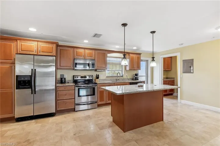 The Del Rey unit kitchen featuring light stone counters, stainless steel appliances, tile floors, a sink, a kitchen island, and pendant lighting