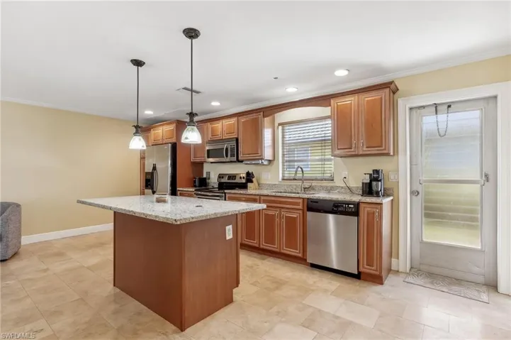 The Del Rey unit kitchen featuring light stone counters, stainless steel appliances, tile floors, a sink, a kitchen island, and pendant lighting