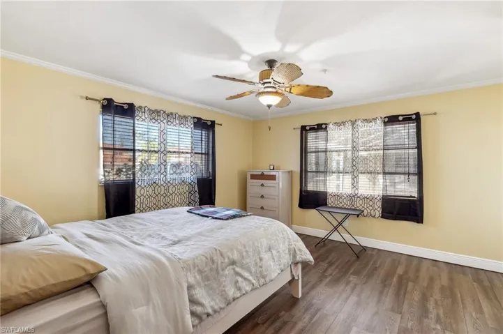 The Del Rey unit Primary Bedroom with dark wood LVT floors, crown molding, ceiling fan, and baseboards