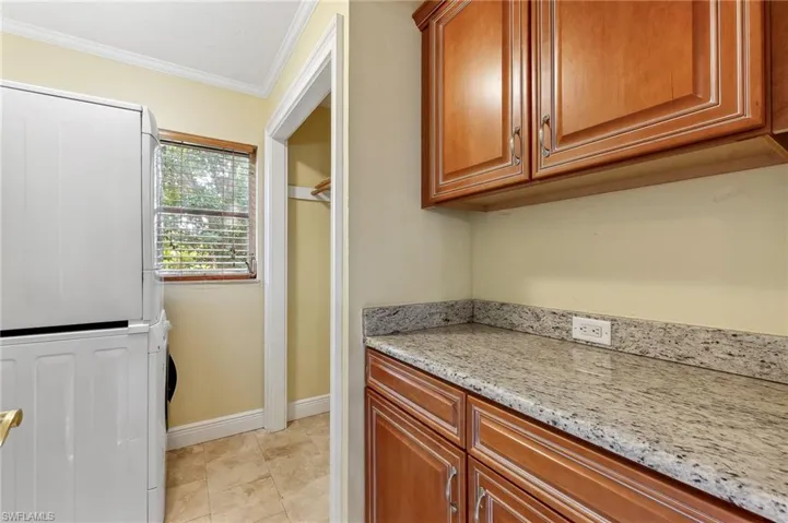 The Captiva unit featuring light tile patterned floors, baseboards, light stone counters, stacked washer / drying machine, storage area,  and crown molding