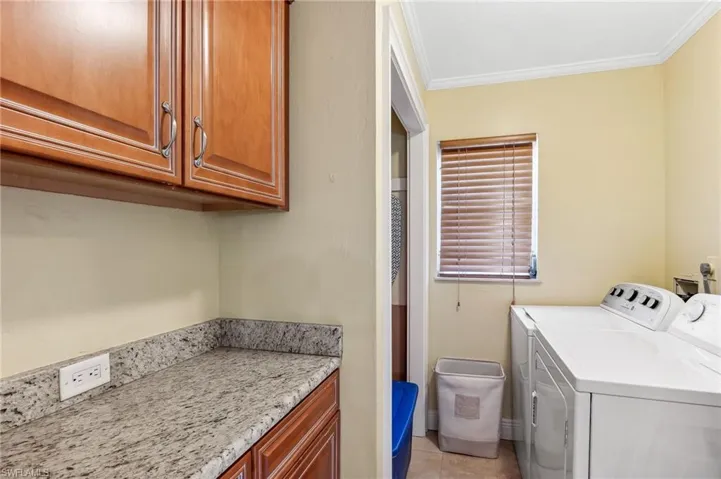 The Del Rey unit laundry area featuring separate washer and dryer, light tile patterned flooring, cabinet space, storage area, and crown molding