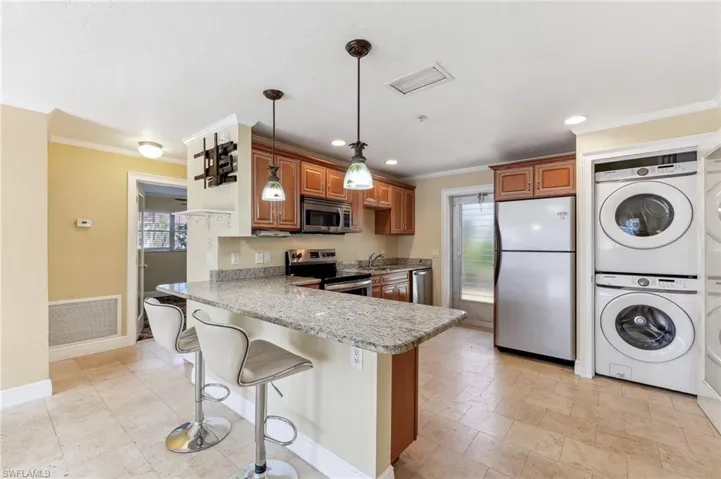 The Aruba unit kitchen featuring tile floors, brown cabinetry, stacked washer / dryer, hanging light fixtures, and stainless steel appliances