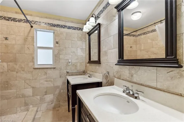 The Del Rey unit full bathroom featuring tile walls, two vanities, a sink, and a walk-in shower.