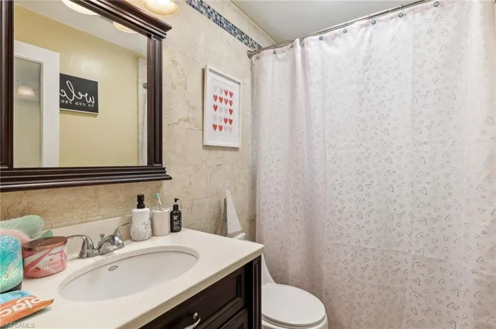 The Boca unit full bathroom with toilet, vanity, tile walls, a walk-in shower and tasteful backsplash
