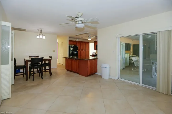 Kitchen with light tile patterned floors, dark countertops, reddish brown cabinets, freestanding refrigerator, and a ceiling fan