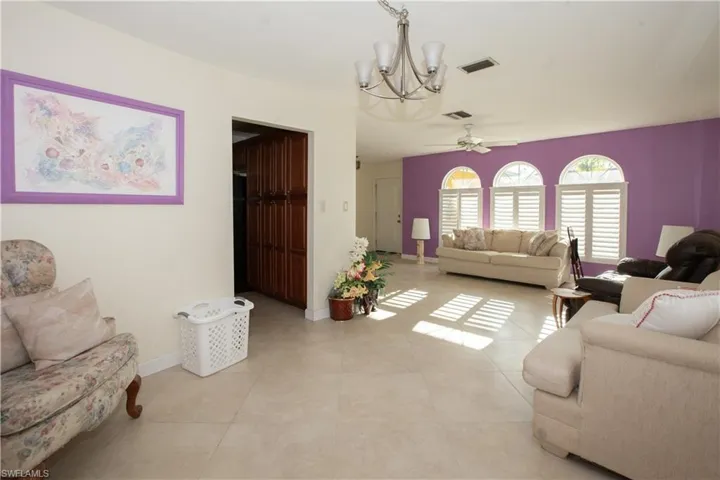 Living area featuring baseboards, light tile patterned floors, visible vents, and ceiling fan with notable chandelier