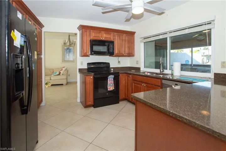 Kitchen featuring light tile patterned floors, dark stone countertops, a sink, ceiling fan, and black appliances