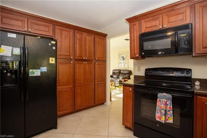 Kitchen with brown cabinets, black appliances, and light tile patterned floors