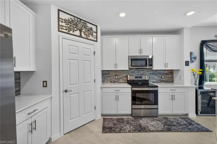 Contemporary kitchen featuring white shaker cabinetry, stainless steel appliances, stacked stone-look backsplash, and recessed lighting