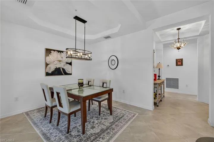 Dining space featuring tray ceiling, contemporary chandelier, tile flooring, and arched entryway with decorative lighting