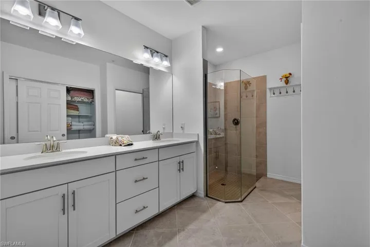 Bathroom featuring a dual vanity with white cabinetry and chrome hardware, a large mirror, and overhead vanity lighting