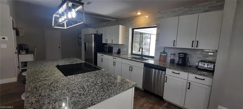Kitchen featuring a kitchen island, a sink, appliances with stainless steel finishes, backsplash, and tile floors