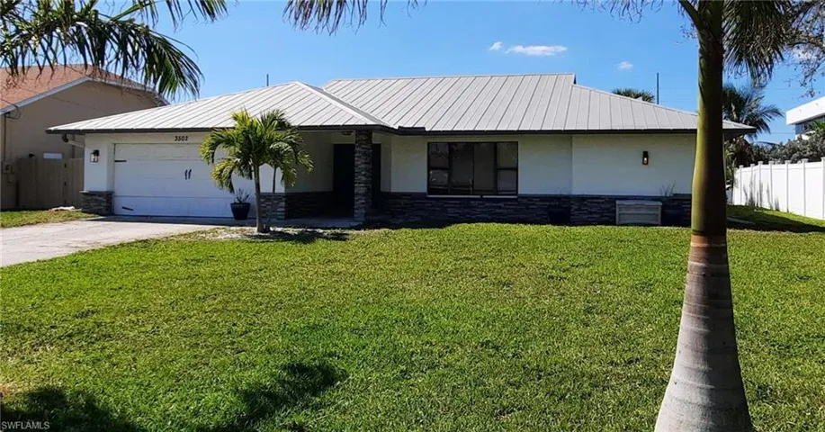 View of front facade with metal roof, an attached garage, fence, and stucco siding