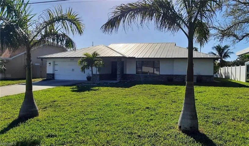 Ranch-style home with metal roof, stone siding, driveway, and stucco siding