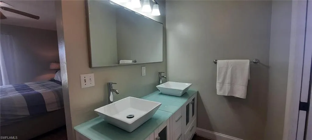 Ensuite bathroom featuring double vanity, ensuite bath, a ceiling fan, and a sink