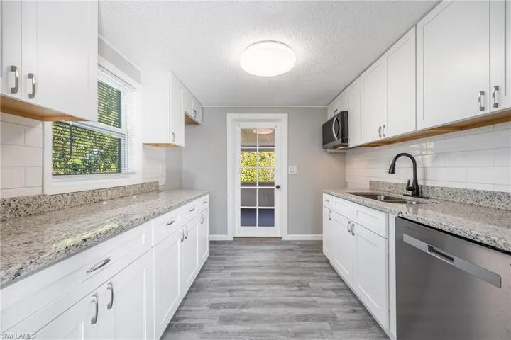 Kitchen with white cabinetry, stainless steel appliances, light stone countertops, and sink